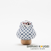 白底藍格紋紙質達摩不倒翁迷你提燈，臉部有戲劇化的黑色、紅色和白色繪畫，放在木製底座上。