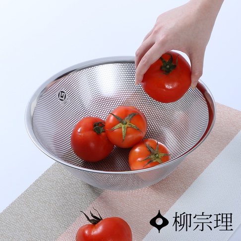 一個不鏽鋼瀝水盆，盆身有細密網孔，盛有四顆紅色番茄，一隻手正在放入第五顆番茄。