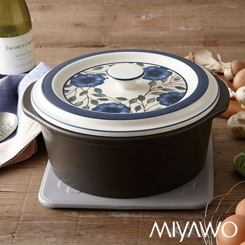 藍色富貴菊圖案的白色陶土鍋蓋，搭配深灰色陶土湯鍋，鍋蓋邊緣有藍色條紋，鍋子放在灰色隔熱墊上。