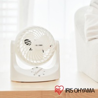 白色IRIS OHYAMA桌上型空氣循環扇TAF-MKM10N，設有可調速的旋鈕，簡約的設計擺放在木質表面上，背景為柔和的白色窗簾與沙發。