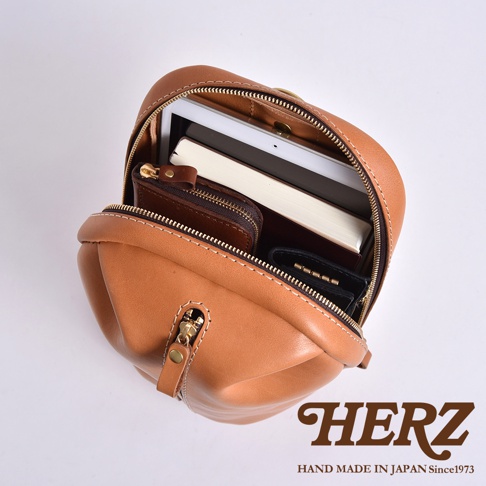 日本HERZ職人手作皮革立體運動斜背包，包內裝有平板、書本、錢包和鑰匙包，展示其收納能力。