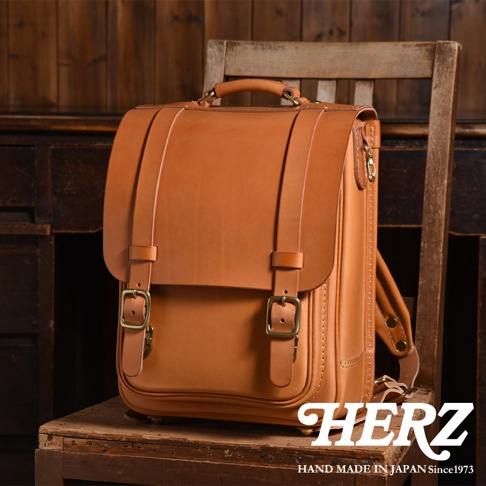 職人手作皮革小學生書包，採用棕色皮革製成，設有雙皮帶扣和提把，風格經典。