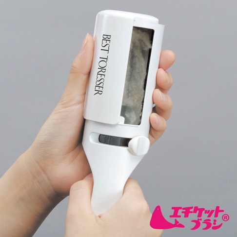 一隻手持白色塑膠製的衣物除塵刷，刷頭部分可見灰色絨毛。刷身側面印有黑色文字「BEST TORESSER」，底部有白色圓形旋鈕。