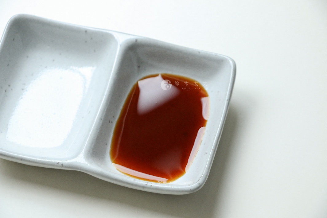 白色陶瓷分格醬料碟，其中一格盛有琥珀色豬排沾醬。