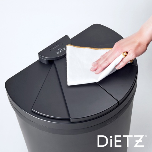 一只手正在用白色布擦拭黑色DustBox30自動感應靜音垃圾桶的頂部蓋板。蓋板為扇形設計，中央有DIETZ品牌標誌和「OPEN/CLOSE」字樣的感應器。