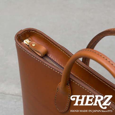 職人手作皮革Organ薄型公事包，焦糖棕色，展示包包頂部拉鍊細節與提把。