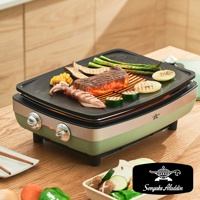 綠色與米色外觀的電烤盤，黑色烤盤上烤著牛排、魷魚、玉米、蘆筍、櫛瓜和洋蔥，散發著炙熱的烤肉香氣。