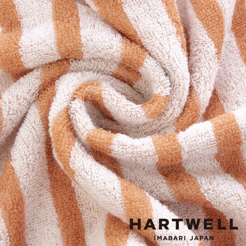 一條由棉製成的薄毛巾，帶有橙色和白色的條紋，質地柔軟，捲曲展示。