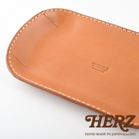 職人手作皮革小物收納盤，淺棕色，邊緣車縫線清晰，皮革表面壓印有「HERZ」及「MADE IN JAPAN」字樣。