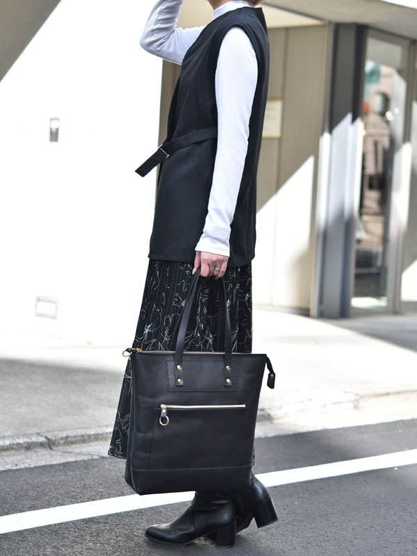 黑色皮革直式拉鍊托特包，具有金色拉鍊和金屬鉚釘裝飾，皮革手柄，外部有一個拉鍊口袋。