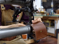 職人手作皮革三折式迷你短夾 (WS-2) 正在工業縫紉機上製作，展示了其光滑的棕色皮革材質、縫線細節和金屬按鈕。