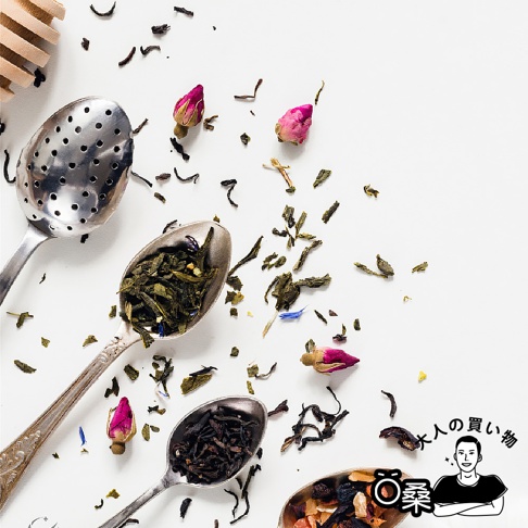 多款茶葉散落在白色背景上，有茶葉、玫瑰花苞和湯匙，其中湯匙裡裝有綠茶、紅茶和蜂蜜風味薄荷茶。