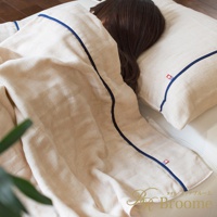 米白色五層紗被子，飾有深藍色滾邊，搭配同色系枕頭，一位女子蓋著被子躺在床上。