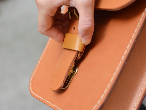 職人手作皮革經典皮扣單肩包（CP-97），採用天然棕色牛皮材質，帶有復古黃銅皮扣設計，手工縫線清晰可見，質感厚實，風格簡約。