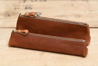 兩個棕色皮革製的三角收納筆袋，配有金色拉鍊和皮革拉環，放置在木質背景上。