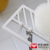 白色塑膠製的直撐款迷你掛勾，附有兩個掛鉤和一個灰色夾子，一旁是白色海綿。