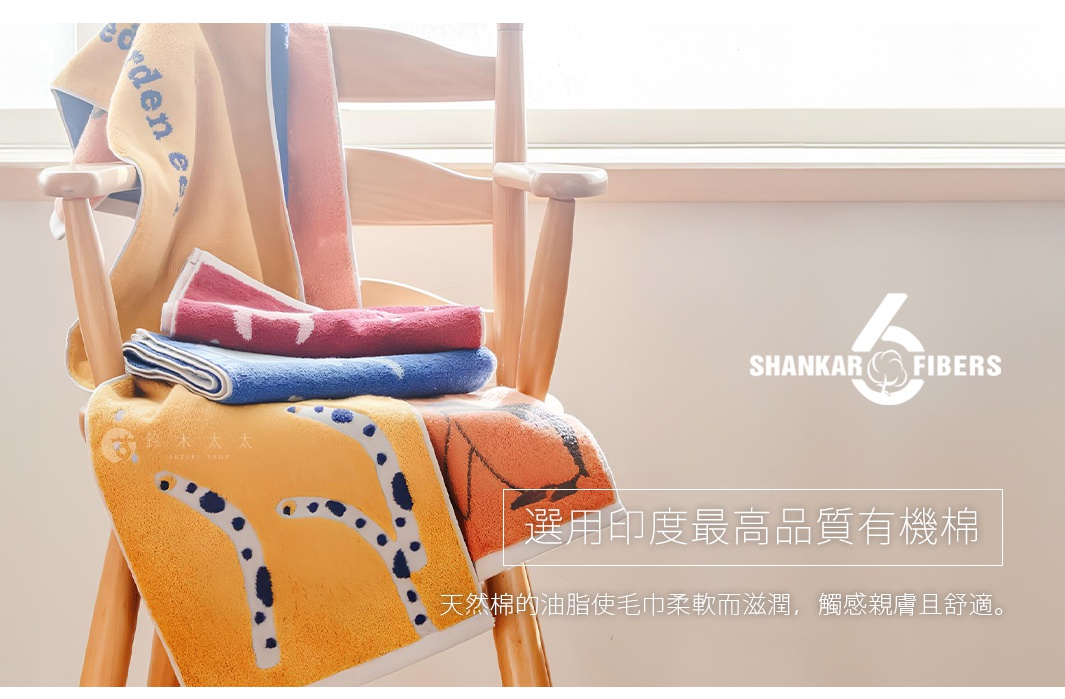 木椅上疊放著幾條毛巾，顏色包含黃色、橘色、粉紅色和藍色。黃色毛巾上有動物（如豹紋）圖案刺繡，粉紅色和藍色毛巾則有簡潔的白色動物圖案。