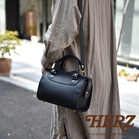 黑色皮革迷你波士頓包，配有金色拉鍊和扣環，可肩背或手提。