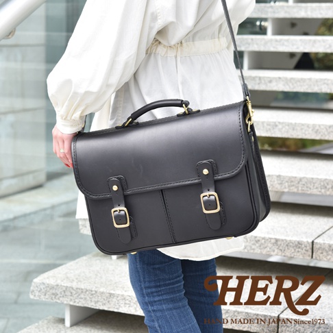 黑色皮革製成的手提單肩包，配有金色搭扣和可調節肩帶，展現精緻的縫線細節。