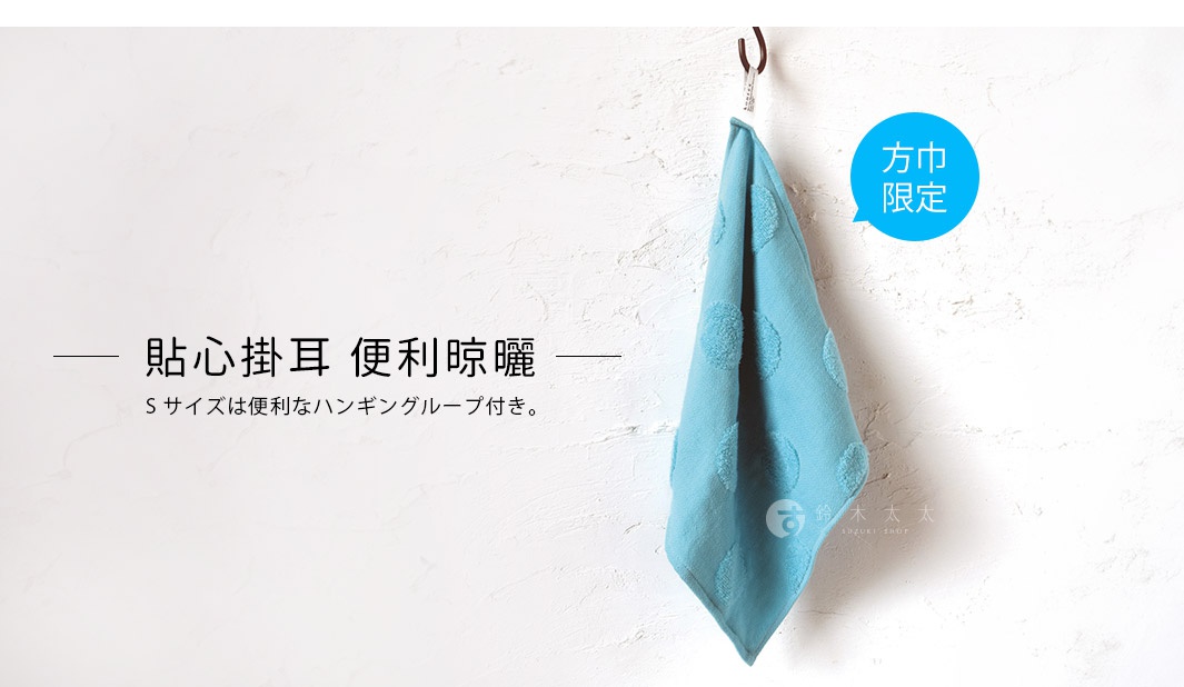 淺藍色紗布方巾，表面有圓點紋路，掛在牆上，背景為白色紋理牆面。