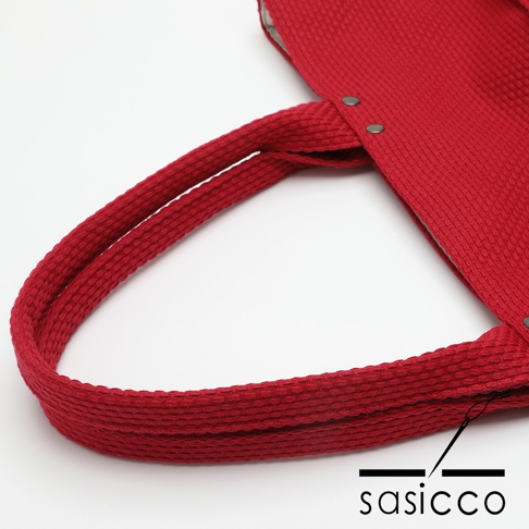 紅色三河木綿刺子織托特包，特寫其寬版提把和包身材質，提把縫有兩顆金屬卯釘。