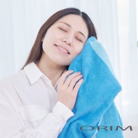 一位女士用柔軟的藍色浴巾輕輕擦拭臉頰，浴巾材質蓬鬆，呈現明亮的藍色調。