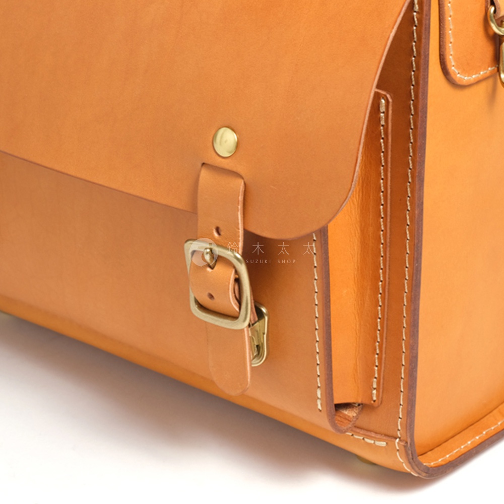 職人手作皮革橫式書包，綴有復古銅色金屬釦環，車縫線精緻，展現皮革的溫潤質感。