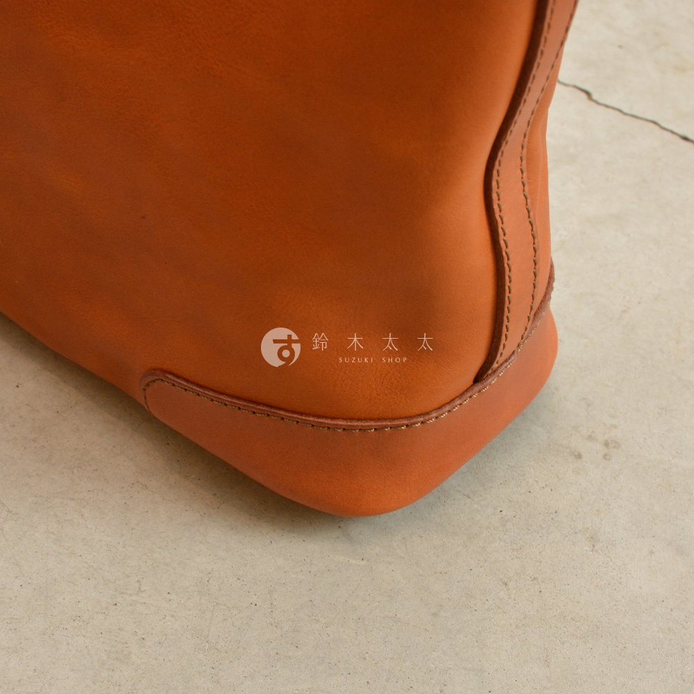 職人手作皮革Organ肩背拉鍊托特包，近拍展示包款底部角落，橘棕色皮革材質，搭配同色系車縫線，簡約而有質感。