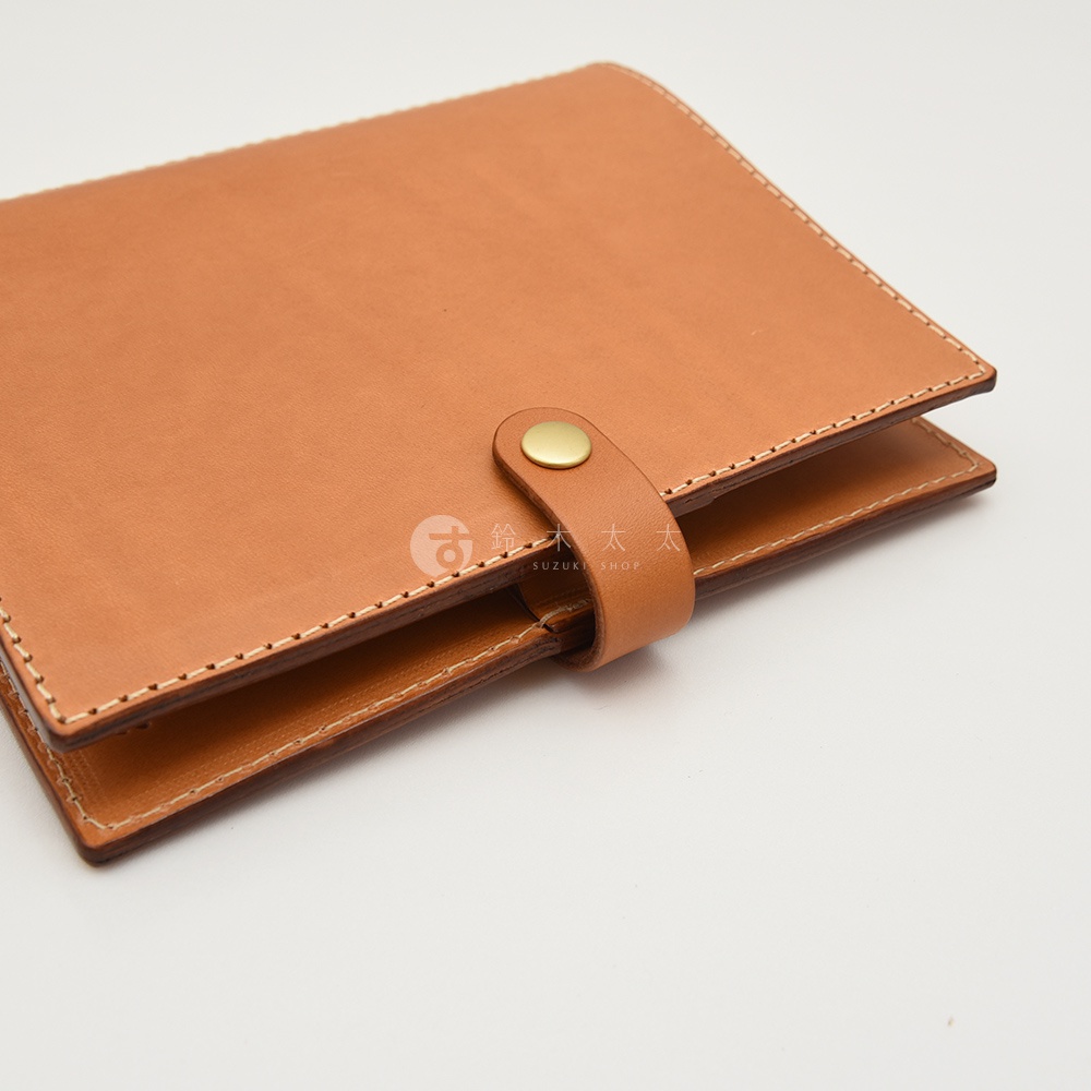 職人手作皮革A5手帳/記事本書套，採用天然皮革材質，呈現溫潤的棕褐色調，車縫線整齊細緻，並以金色按扣作為固定設計。