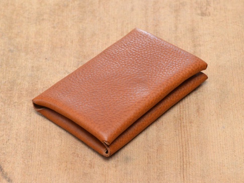 棕色皮革製成的雙開卡片收納夾，表面有細緻紋理，置於木紋背景上。