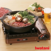 銅色雙重防風卡式爐 KZ-2，爐身側面有圓形旋鈕和標誌，上方放置著黑色鍋子，鍋內有牛肉、豆腐、香菇、蔬菜和粉絲，冒著熱氣。