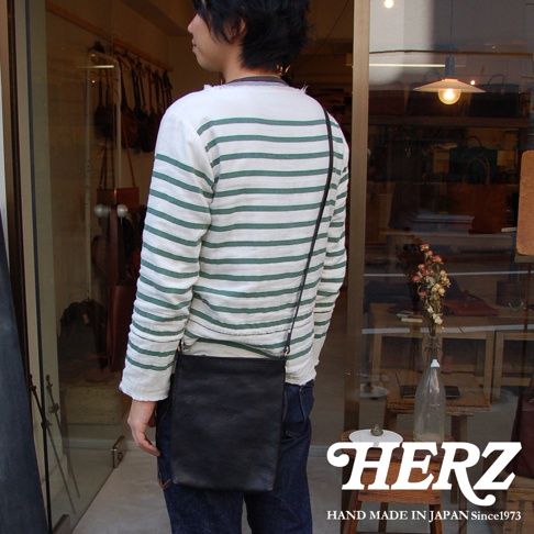 職人手作黑色皮革Organ肩背小方包，簡約設計，搭配綠色條紋長袖上衣與牛仔褲，展現休閒風格。