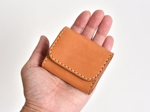 一只手掌托著一個棕褐色皮革雙折收納零錢包，包身有米白色縫線裝飾。