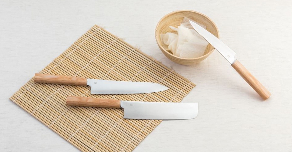 兩把Yuri / Petit knife水果刀，均帶有淺木色手柄，刀身為銀色金屬。一把刀呈細長形，另一把為方形。兩刀皆置於竹製蓆子上，旁邊有一個裝有白色食材的木碗。