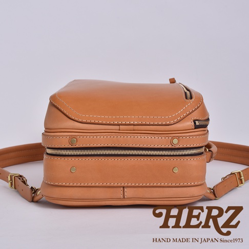 職人手作皮革兩用商務後背包 R-33，採用溫潤的駝色皮革，雙層結構設計，搭配金色拉鍊與金屬扣環，展現質感與實用性。