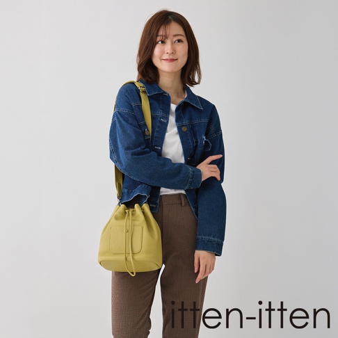 itten-itten 品牌 BOLLA 義大利皮革束口水桶包，模特身穿丹寧外套與格紋長褲，斜挎黃色水桶包。