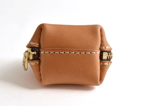 一個棕色皮革製成的貝殼造型零錢包，兩側有黃銅拉鍊，縫線為米白色，呈現簡約復古風格。