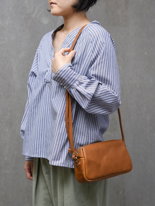 側背一個棕色皮革拉鍊單肩包，包包款式簡約，材質呈現自然紋理，搭配條紋上衣和寬鬆長褲。