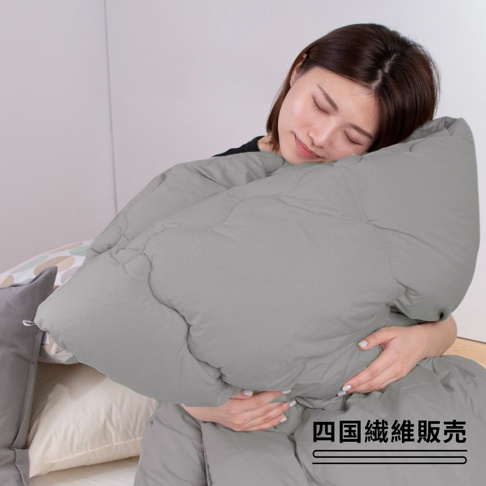 一位女性抱著一件灰色的雙人被，被子呈現蓬鬆的填充感，表面有縫線分格，材質看起來柔軟。