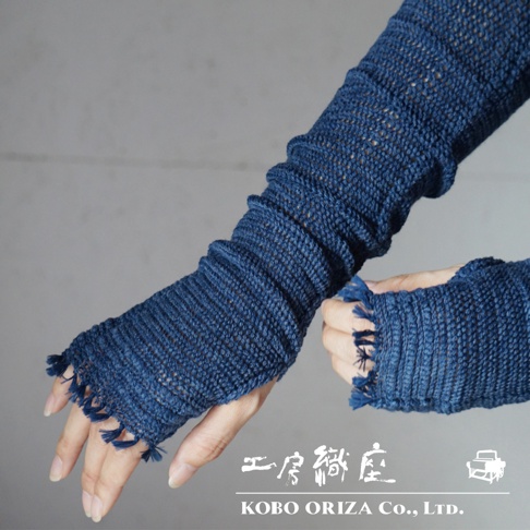 兩隻手臂各穿戴一對深藍色、網眼織紋的輕柔有機棉遮陽袖套，袖套具有縮褶設計，袖口處有流蘇裝飾。