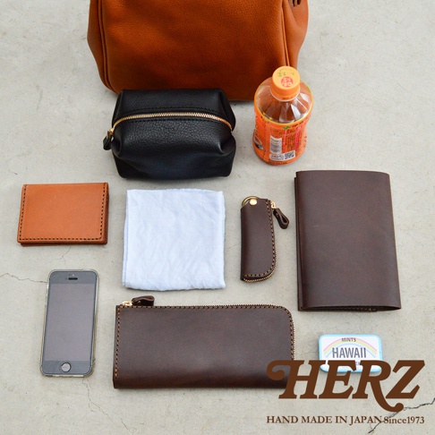 職人手作皮革Organ方形口金托特包 G-55，展示內容包含咖啡色皮革托特包、黑色皮革化妝包、棕色皮革名片夾、白色布巾、棕色皮革鑰匙包、棕色皮革長夾、手機及一瓶飲料。