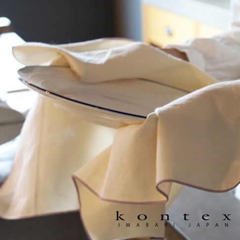 一張特寫照片展示了 KONTEX 今治和紙有機棉廚房拭巾，材質呈現自然柔和的米白色，邊緣點綴著細緻的淡粉色車縫線，布料輕盈覆蓋在平滑的盤子上，營造出溫潤舒適的居家生活質感，底部標註有品牌字樣與日本今治產地資訊。