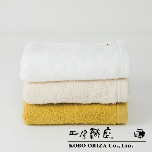 堆疊的今治毛巾，顏色從上到下分別為白色、米白色和芥末黃。毛巾質地柔軟，有細緻的絨毛感。