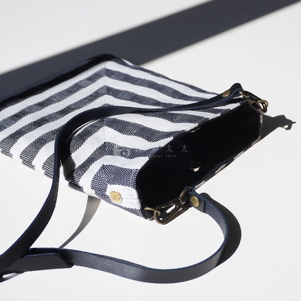 BAN INOUE 斑馬條紋麻布散步斜背包，特寫視角，展示了包包的麻布材質、黑白斑馬紋路，以及皮質背帶和金屬扣環細節。
