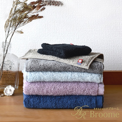 堆疊的今治長毛巾，從上到下顏色分別是：黑色、淺灰色、灰色、淺藍色、淡紫色和深藍色。部分毛巾帶有紅藍色標誌。