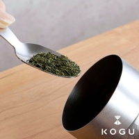 日製18-8不鏽鋼錘目紋茶葉罐，附有茶匙，茶匙中裝有綠色茶葉，準備放入罐中。