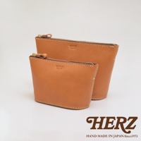 兩款不同尺寸的職人手作皮革三角收納包，皆為淺棕色皮革材質，配有金色拉鍊及品牌壓印。