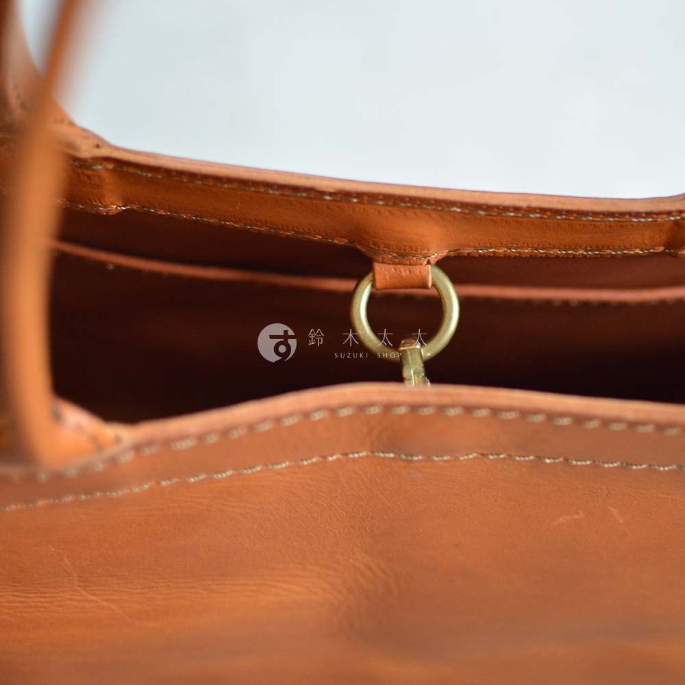 職人手作皮革Organ肩背托特包的內部細節，展示了品牌標誌與金屬扣環，以及縫線工藝。