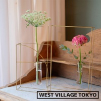 兩款簡約黃銅書本造型掛擺兩用花器，分別搭配一束綠色羽毛狀小花和一朵粉紅色花朵，置於透明玻璃試管中，展現現代設計感。