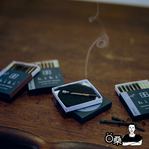 深木質調香氛火柴禮盒，內含三組精緻火柴，其中一組已點燃並散發細緻煙霧，置於白色方盒內。另有兩盒深綠色紙盒包裝的火柴，部分火柴頭清晰可見。